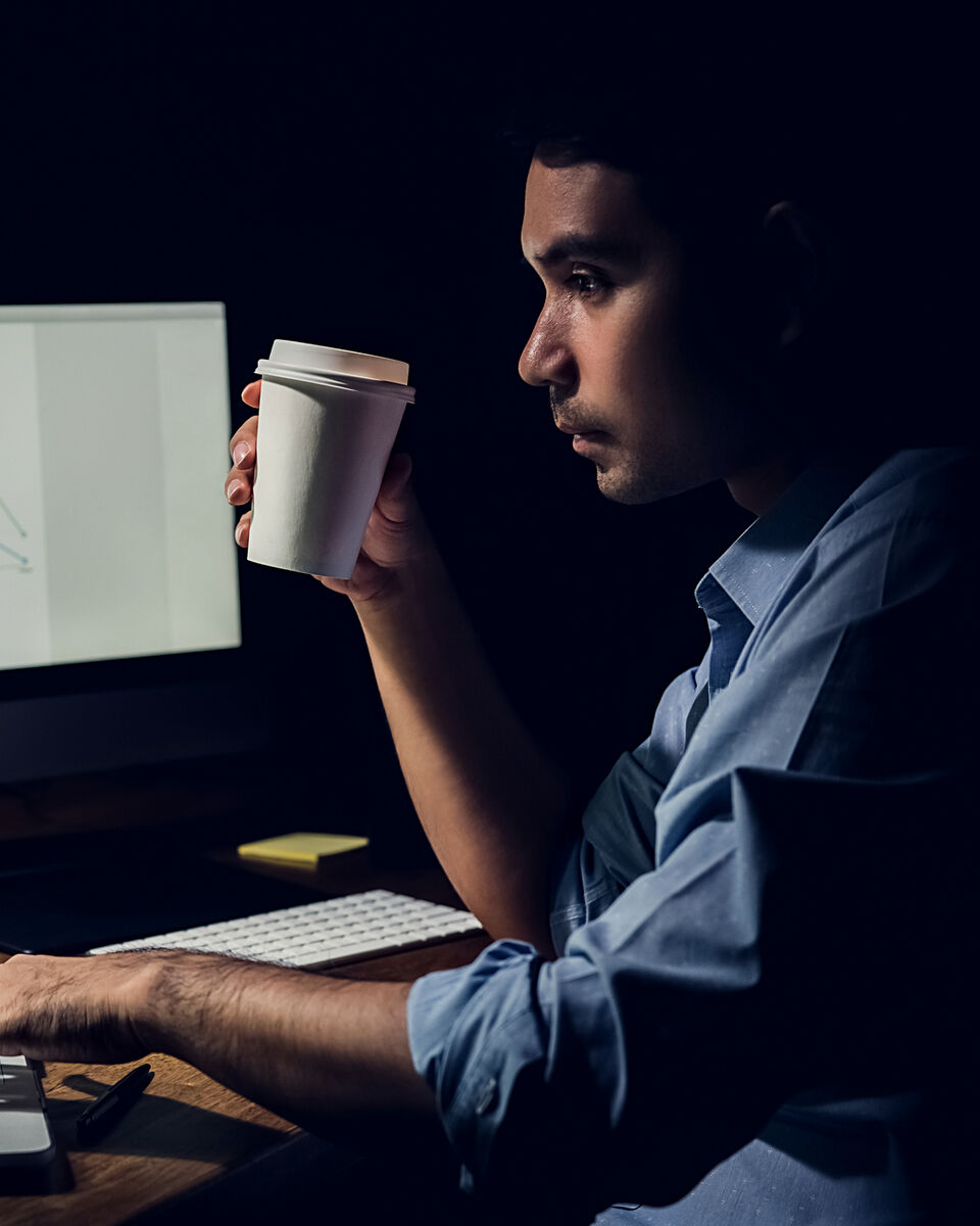 A man at a computer early in the morning, holding a cup of coffee