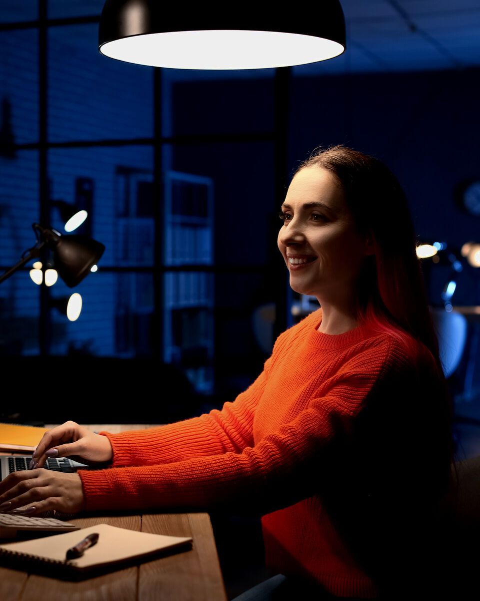 A woman at her desk working at a computer under a lamp